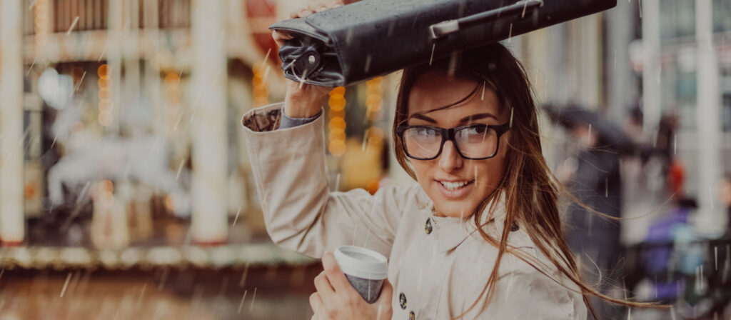 Eine Frau schützt ihr Gesicht mithilfe einer Aktentasche vor dem Regen. Symbolisch steht dieses Bild für den Schutz, den eine Elementarschadenversicherung Unternehmen im Schadensfall gewährt.